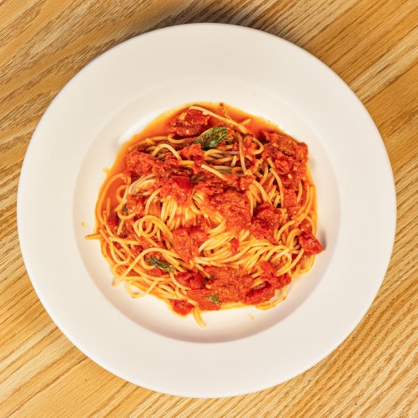 Spaghetti with chunky tomato sauce and basil on a white plate, on a wooden table.