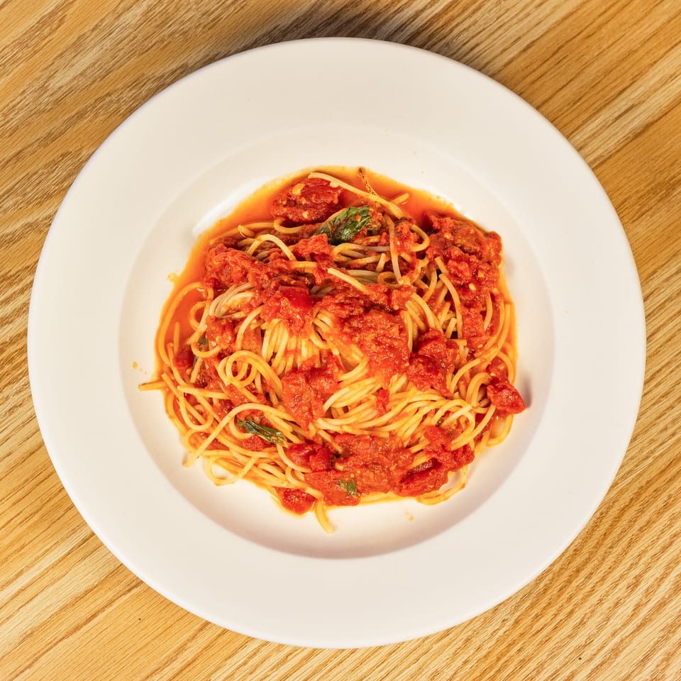 Spaghetti with chunky tomato sauce and basil on a white plate, on a wooden table.