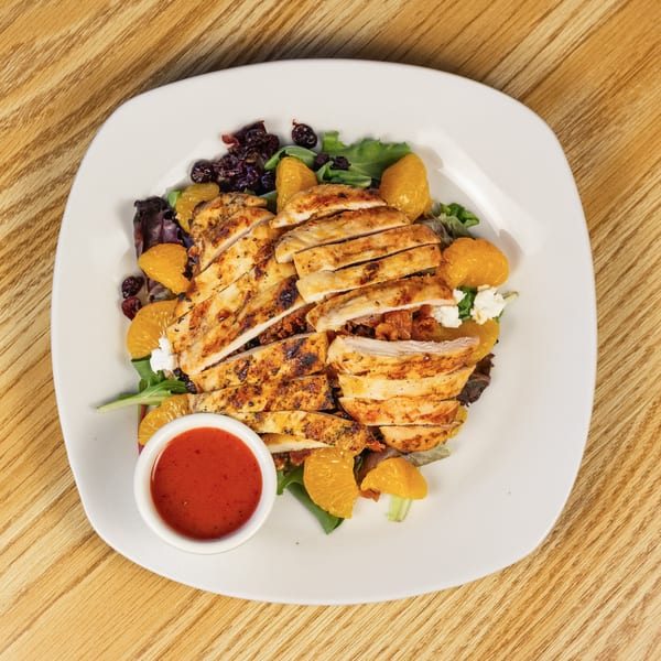 Grilled chicken salad with mandarin oranges, cranberries, feta, and red dressing on a white plate.