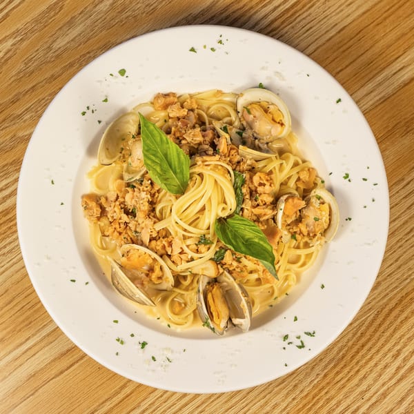 Linguine pasta with clams in a creamy sauce, garnished with fresh basil on a white plate.