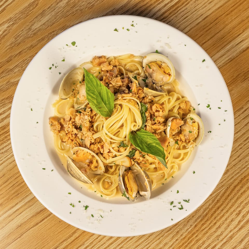 Linguine pasta with clams in a creamy sauce, garnished with fresh basil on a white plate.
