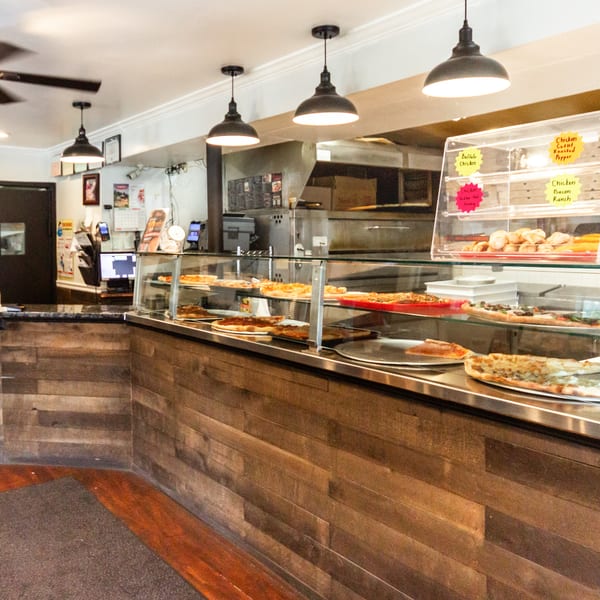 Long pizza display counter showcasing various fresh pizzas and baked goods in a casual restaurant.