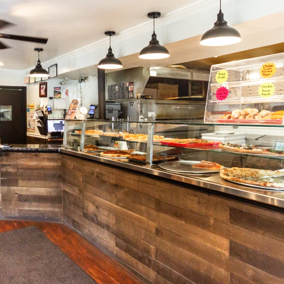 Long pizza display counter showcasing various fresh pizzas and baked goods in a casual restaurant.