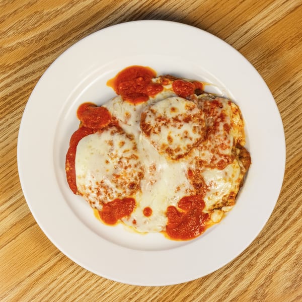 Baked dish covered in melted mozzarella cheese and red marinara sauce on a white plate.