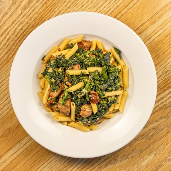 Penne pasta with sausage and broccoli rabe on a white plate, on a wooden table.