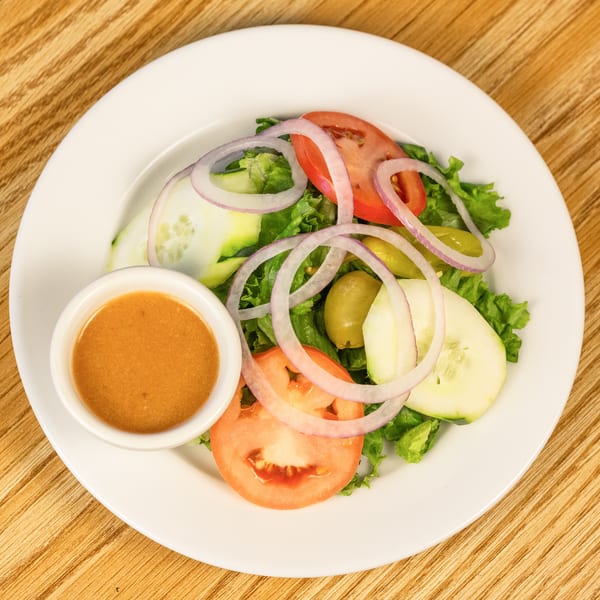Fresh garden salad with lettuce, tomatoes, cucumbers, red onions, olives, and a side of dressing.