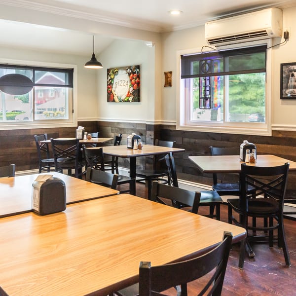 Empty restaurant dining area featuring light wood tables, dark chairs, and rustic wood paneling.